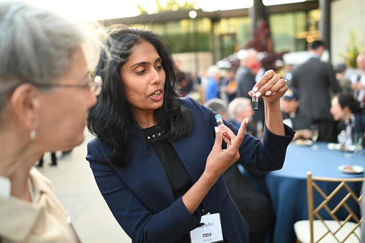 Color photo of Sapna Puri showing small test tubes to a person looking on with interest.