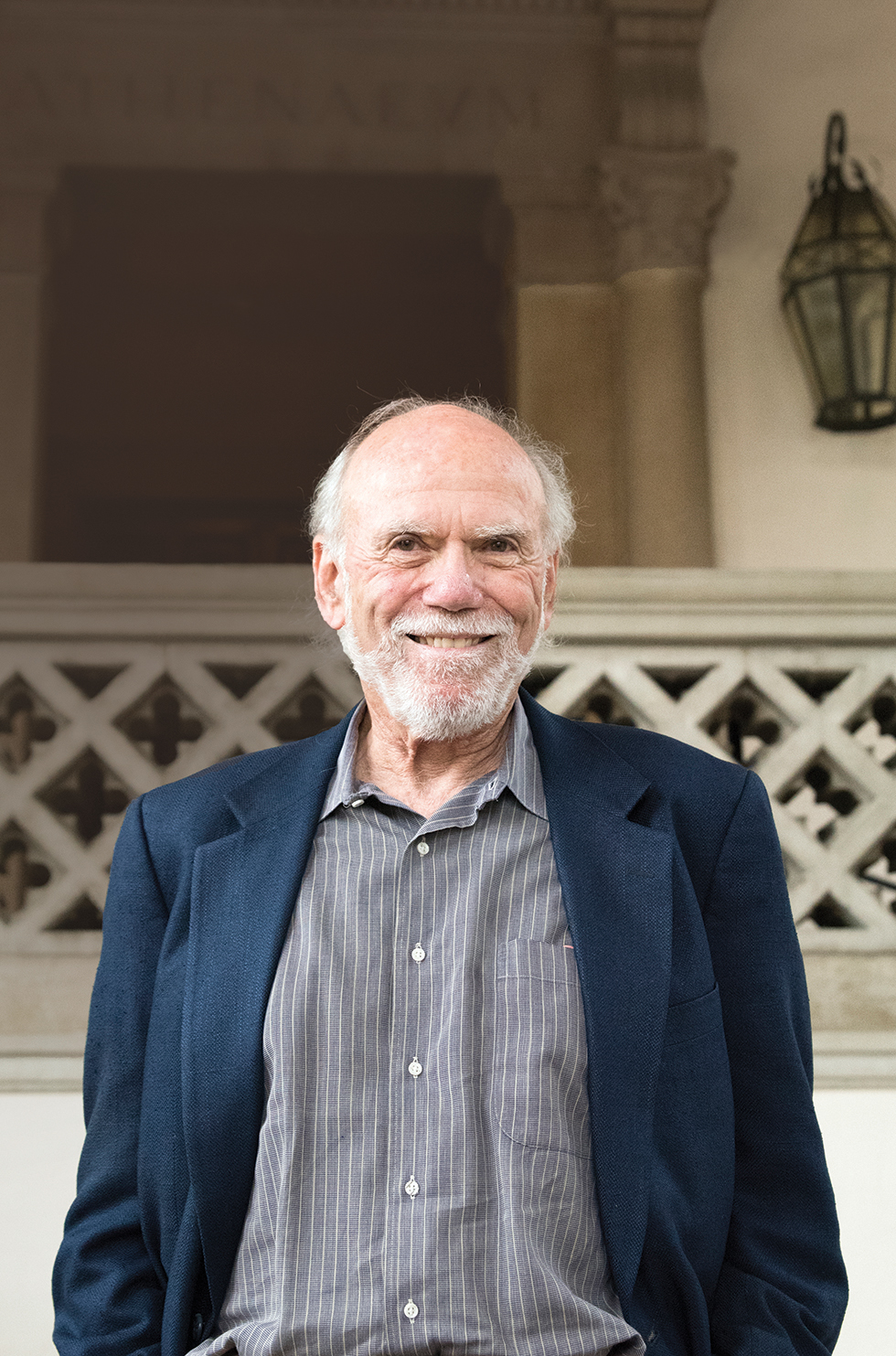 Photo of Barry smiling in a blue jacket  in front of an arch and balcony.