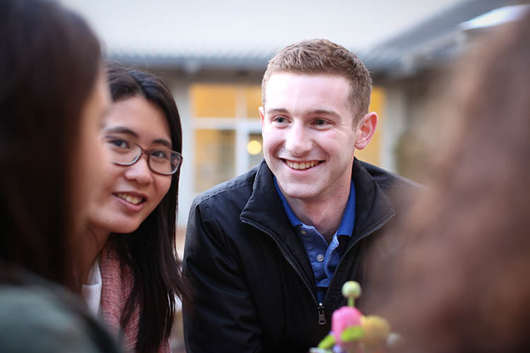 Photo of one female student with glasses and long black hair and a male student in dark jacket, both in conversation with two others.