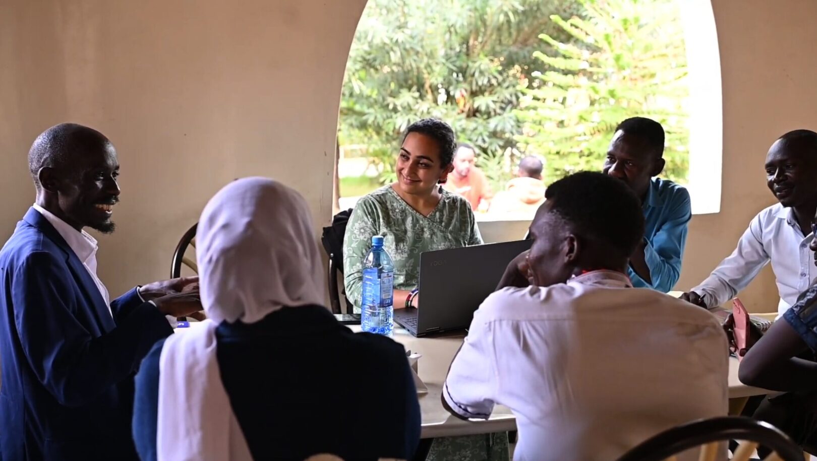 Photo of Bhavya sitting at a table with at least six other people engaged in conversation.