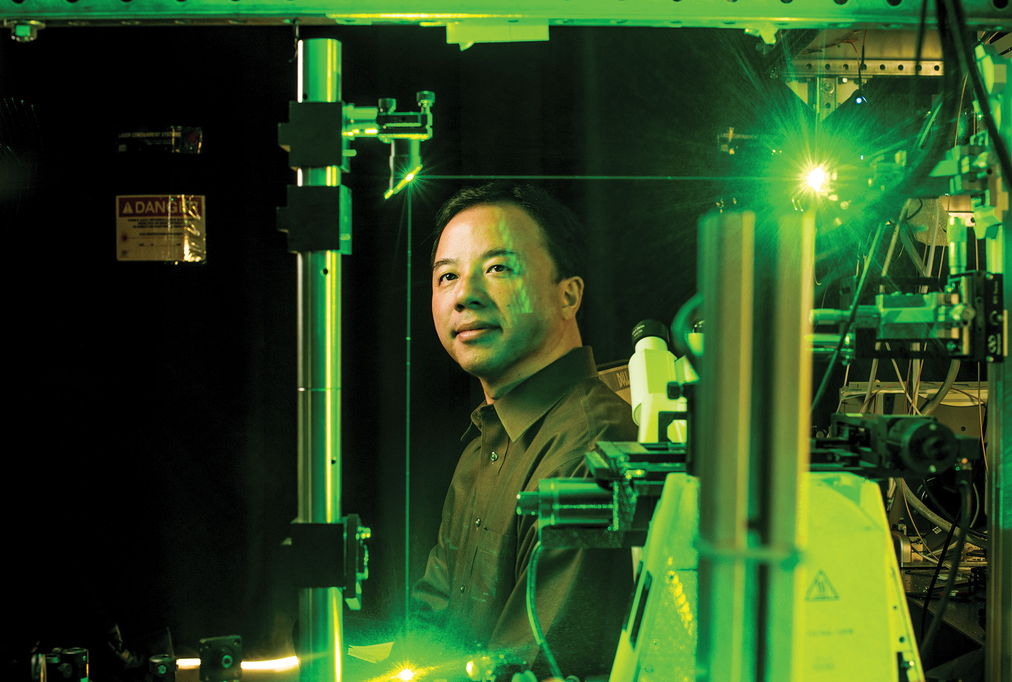 Photo of Dr. Xiang Zhang in his lab, the only light a green beam that casts the whole room in its color