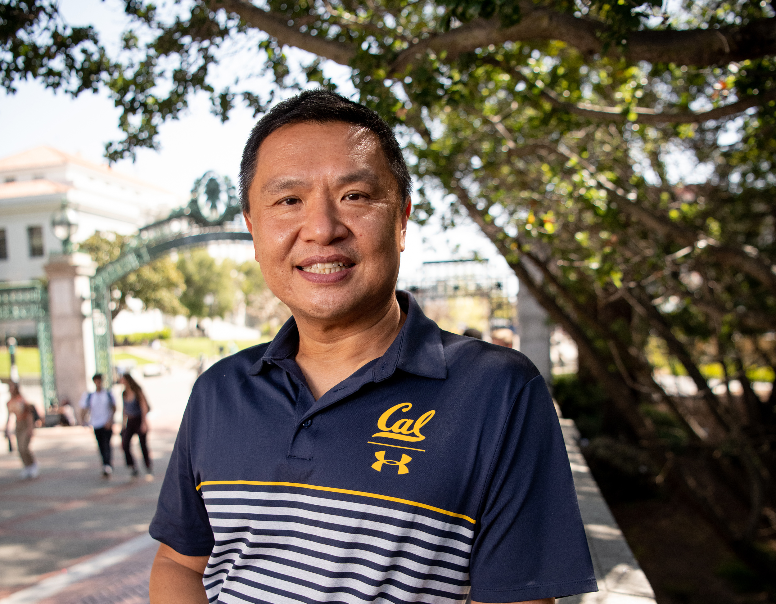 Photo of Charles in a striped Cal shirt, leaning against a wall in front of Sather Gate