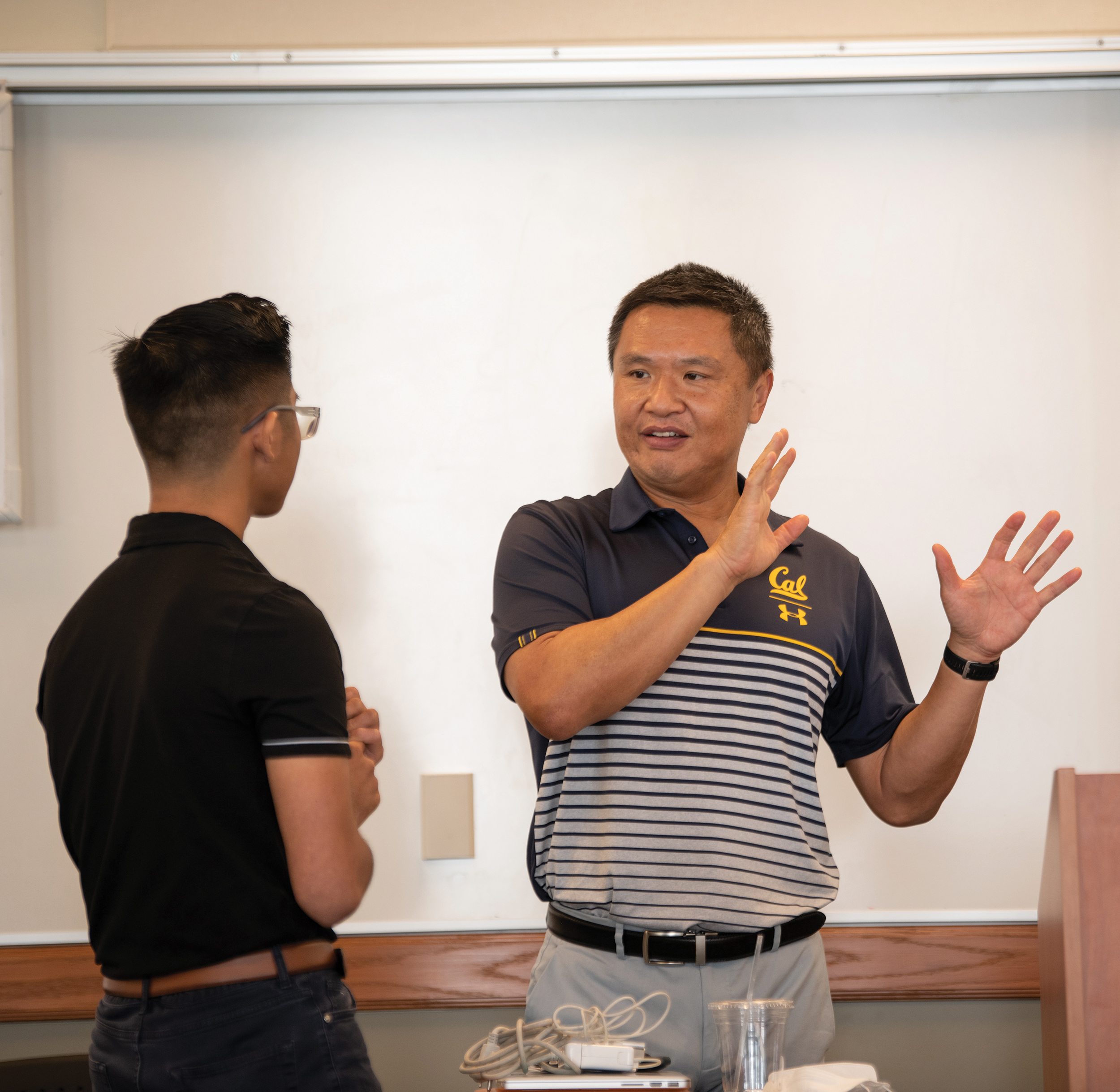 Photo of Charles in a blue striped Cal shirt talking to a student, who has his back turned to the camera and is wearing a dark colored shirt.