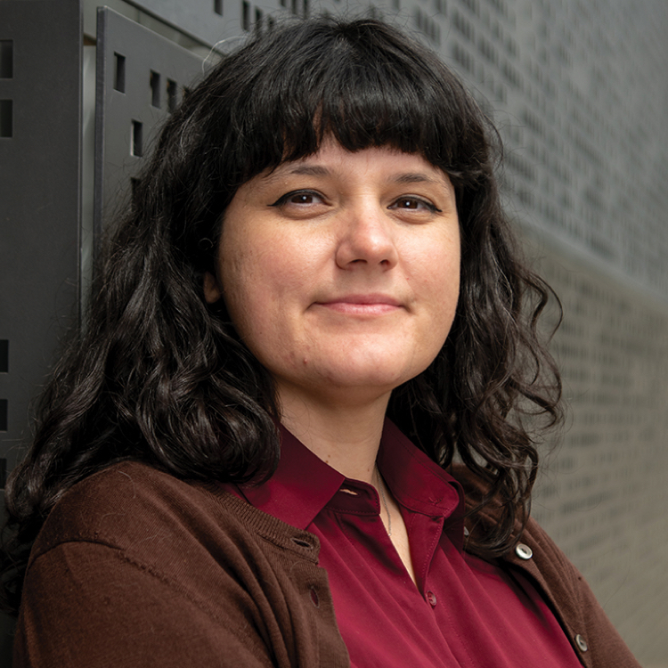 Photo of Ciera leaning against a textured wall wearing a red shirt and brown cardigan.