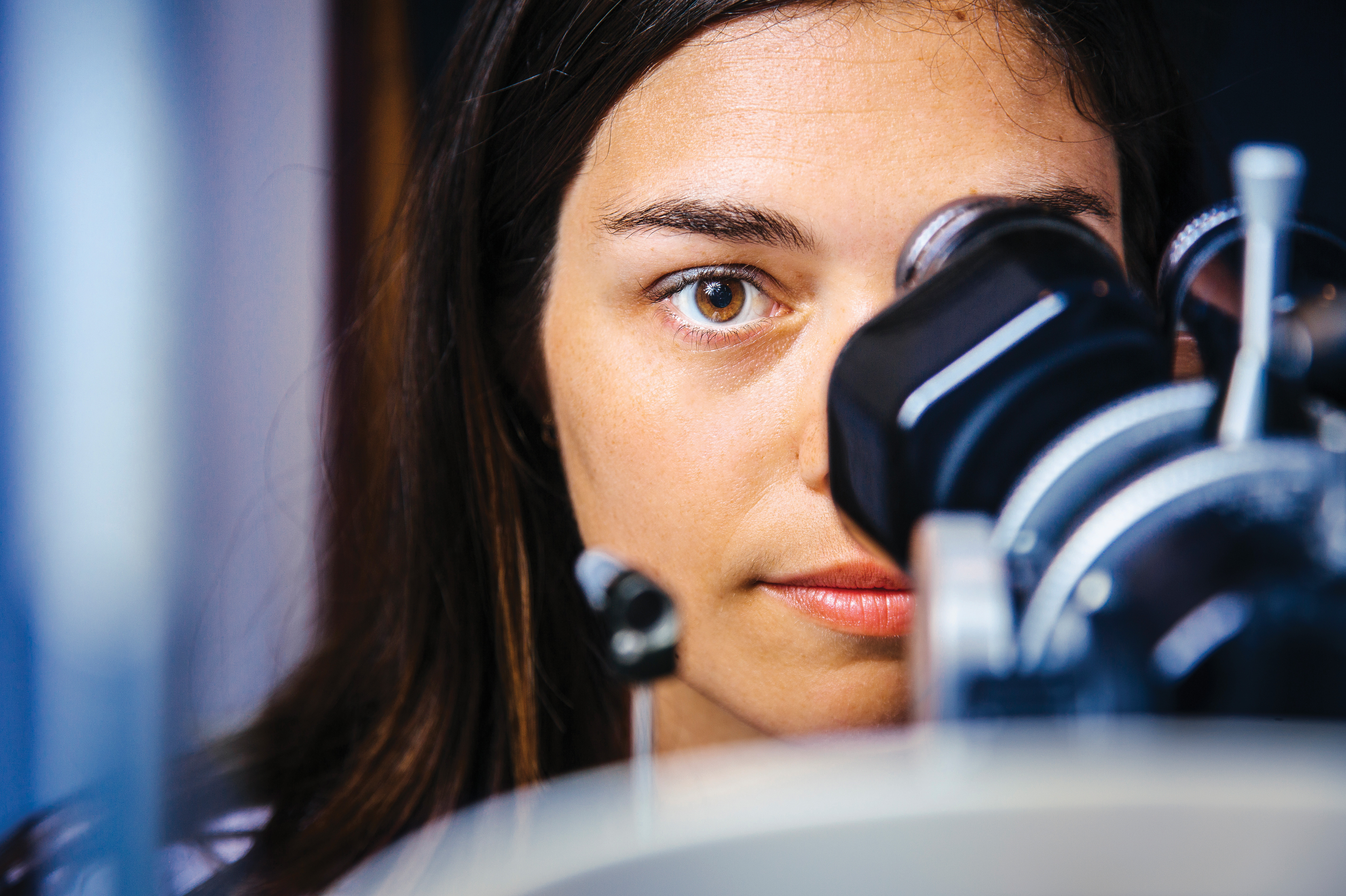 Photo of a young woman looking through the viewer on a piece of optometry equipment.