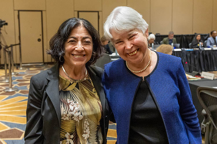 Photo of Jennifer in a brown and cream-colored floral top and dark jacket with her arm around Carol, who's wearing a black top and blue jacket. Both are smiling.