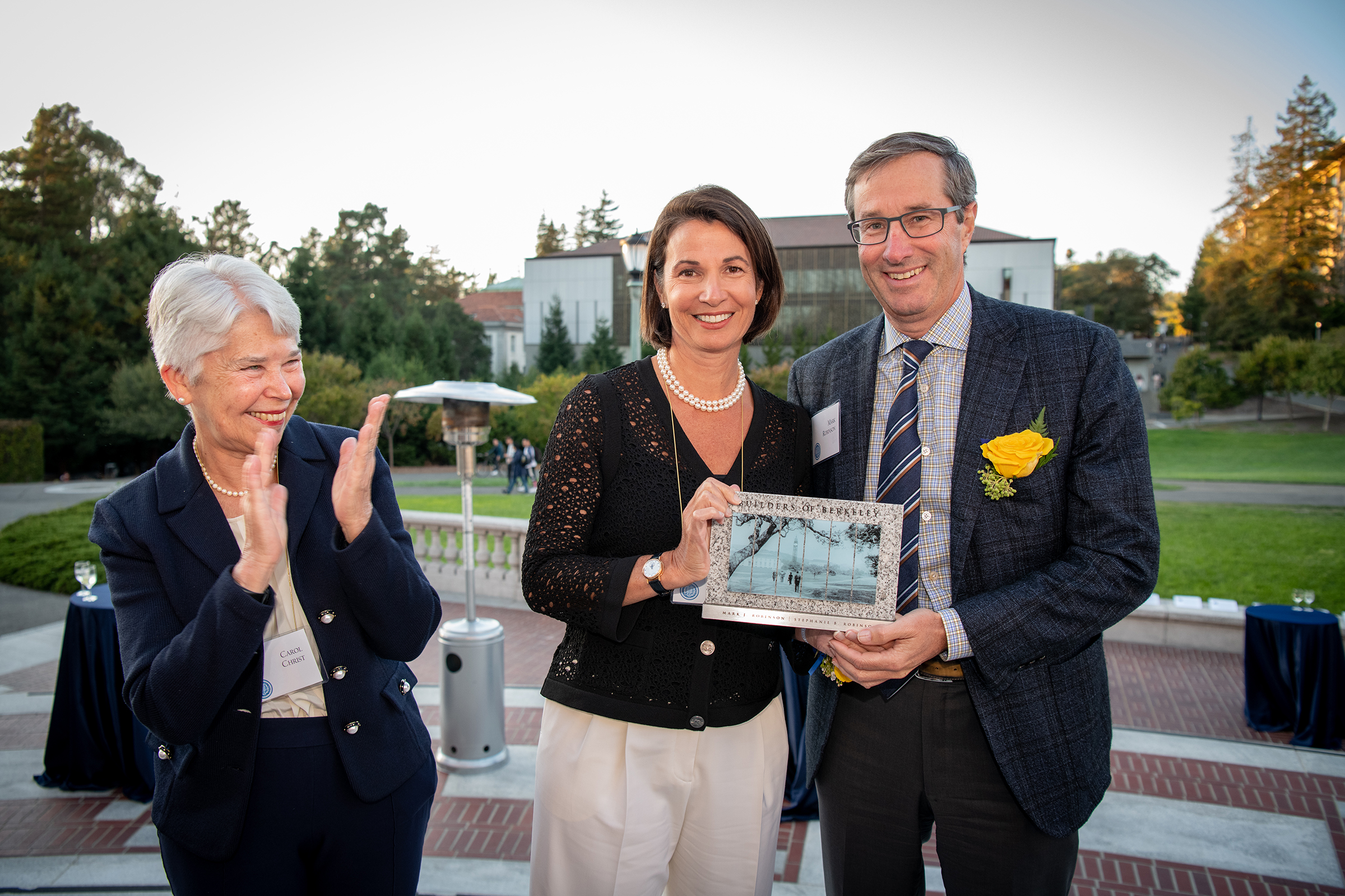 Photo of Chancellor Christ clapping and looking warmly upon Stephanie and Mark, who are holding a plaque.