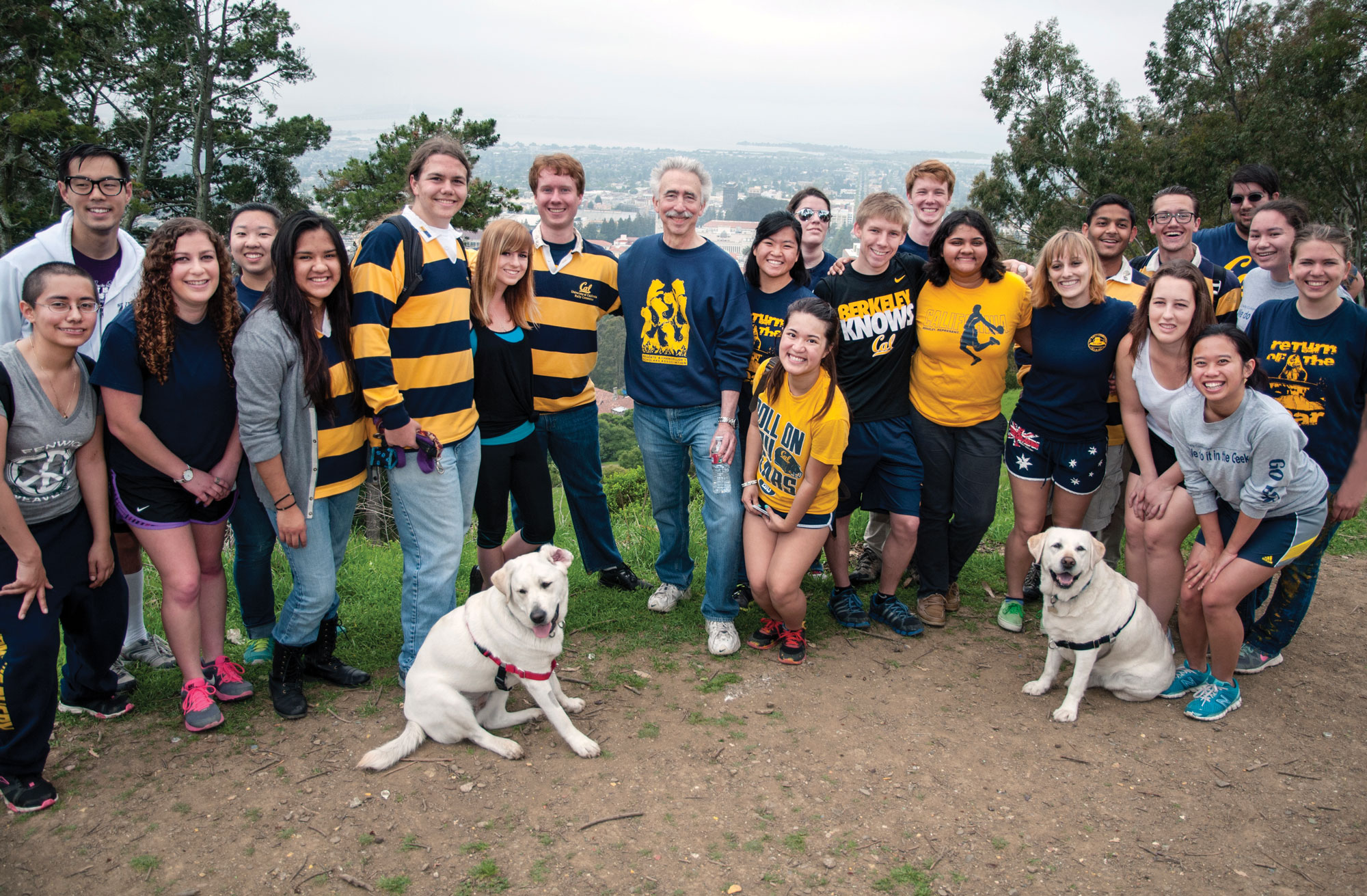 Photo of the chancellor and about 15 students, most wearing blue and gold attire, with a foggy city in the backgound.