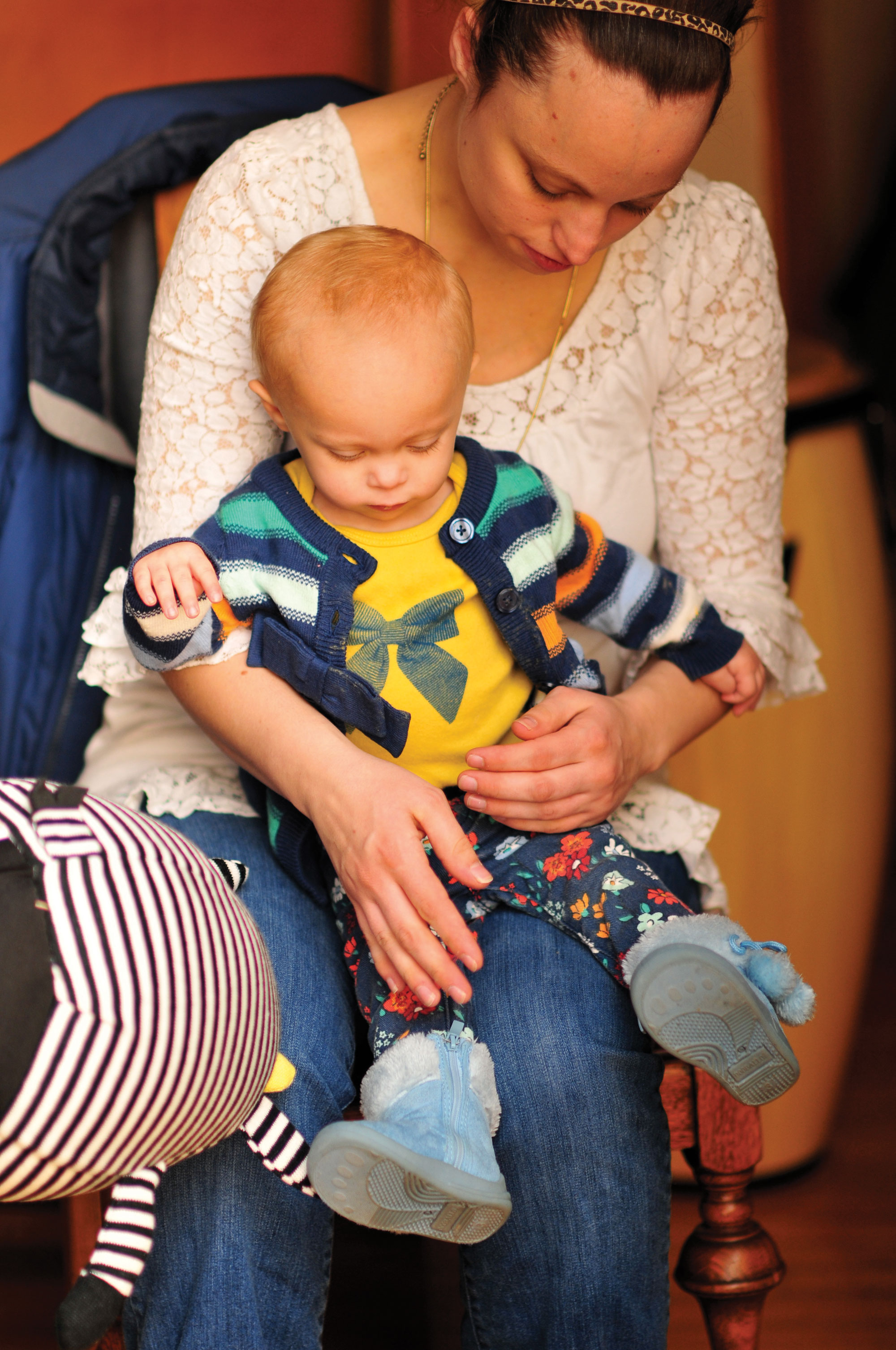 Photo of a young woman holding a colorfully dressed baby in her lap, both looking down