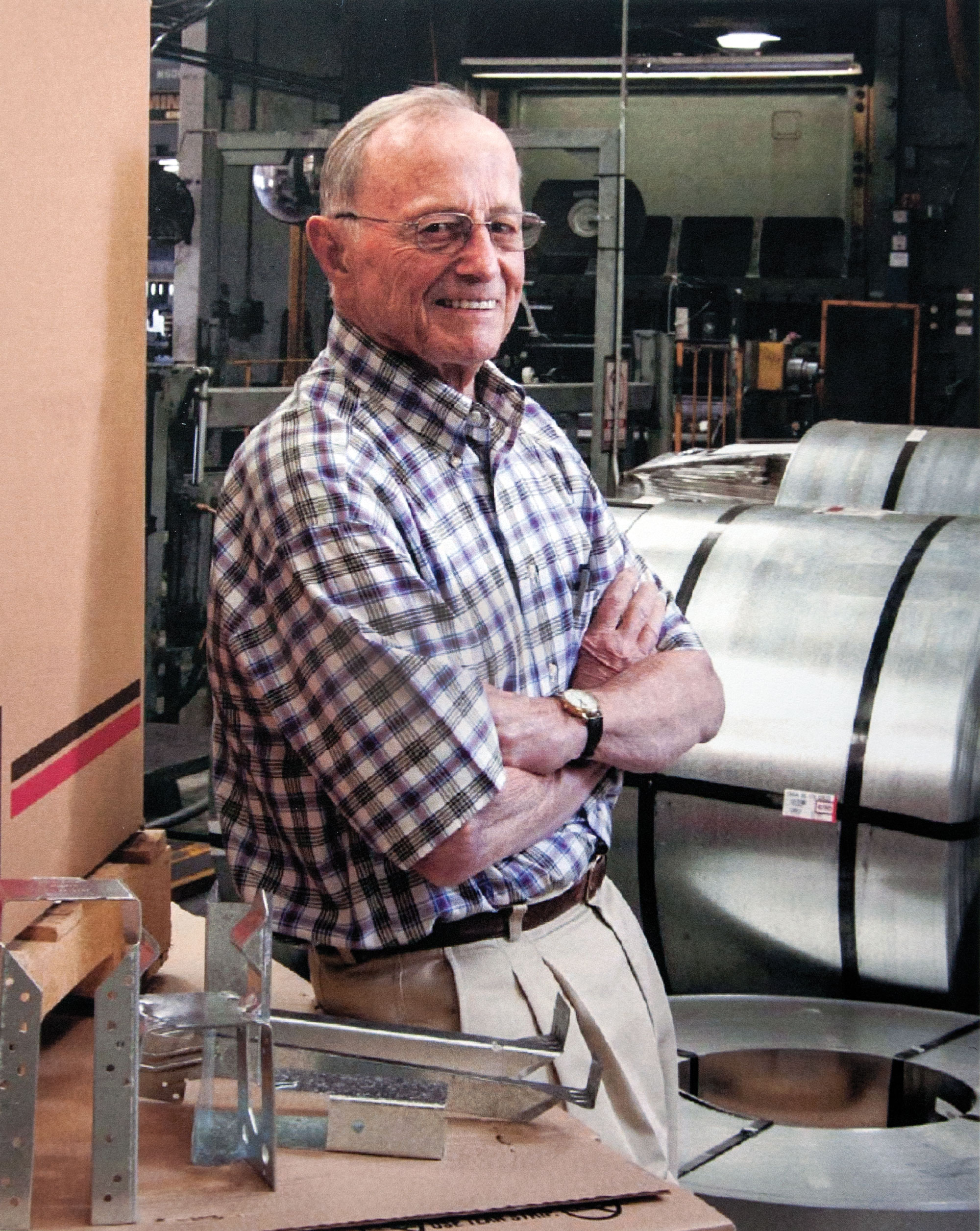 Photo of Barclay Simpson, smiling into the camera, arms crossed, standing in a workshop