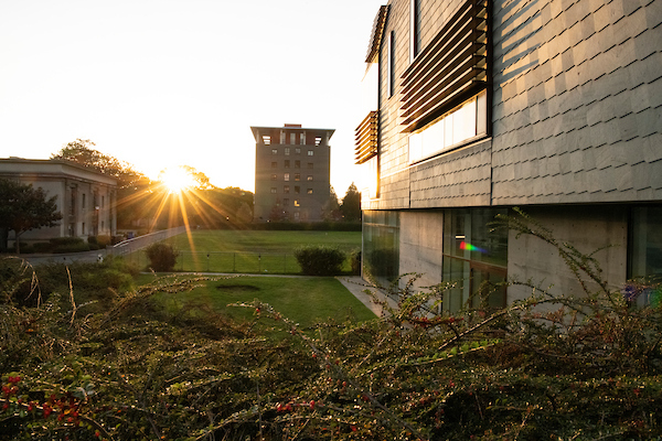 Photo of the setting sun in a blast of golden light over three buildings on campus.