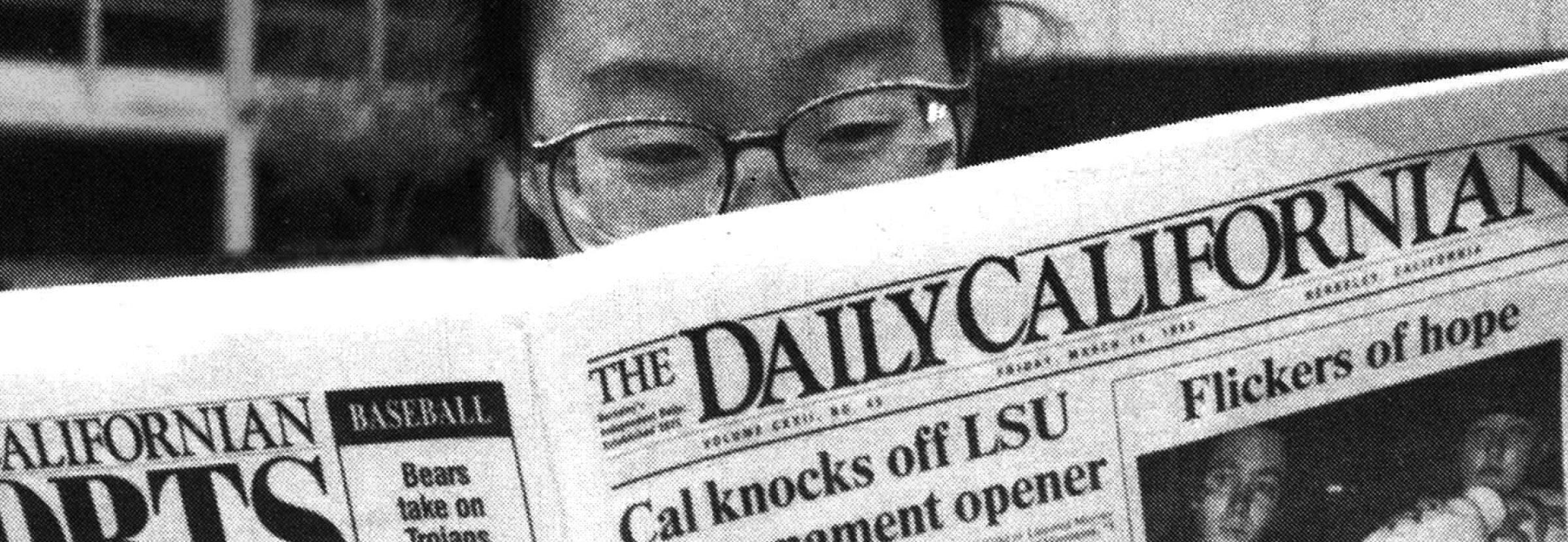 Black-and-white photo of a person reading the Daily Cal newspaper, their spectacles just visible over the paper.