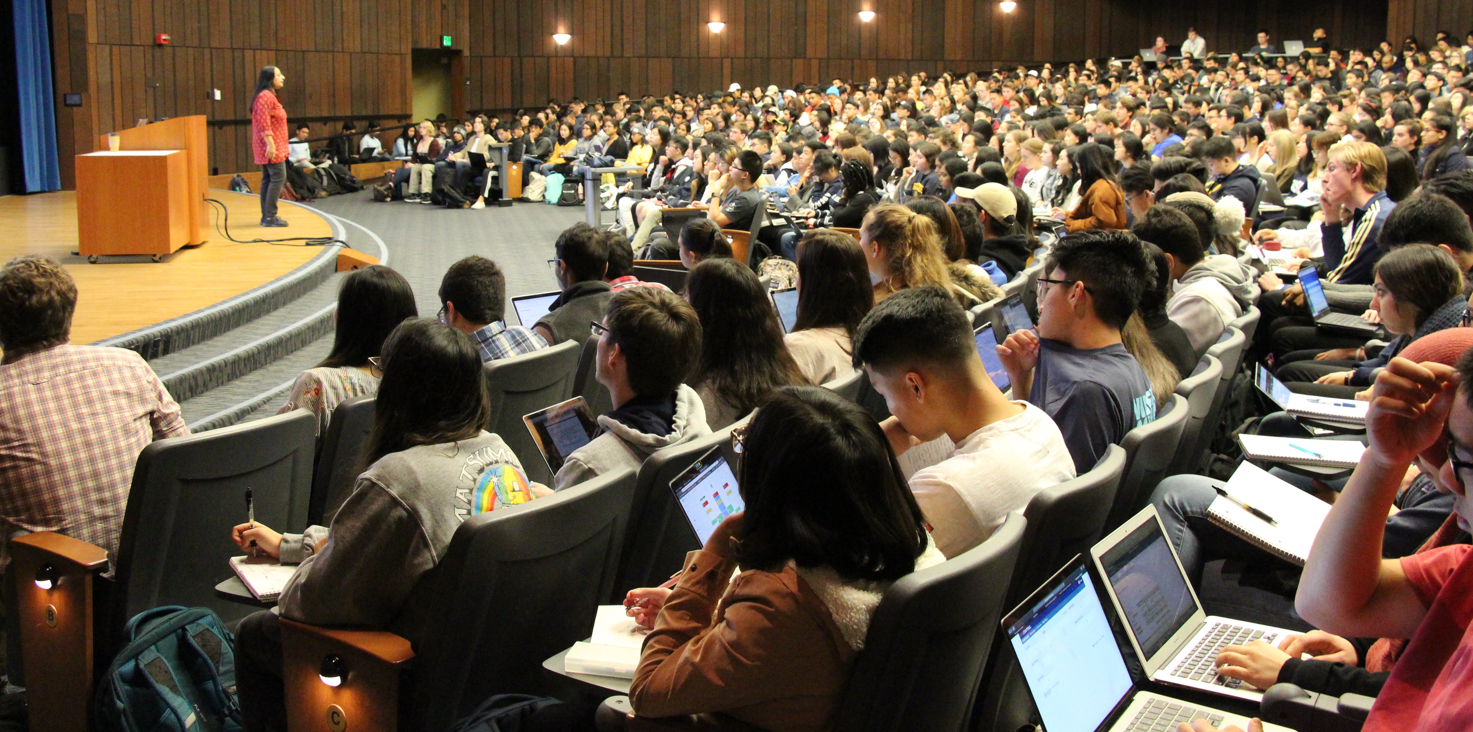 Photo of a full lecture hall, taken from the left side of the back