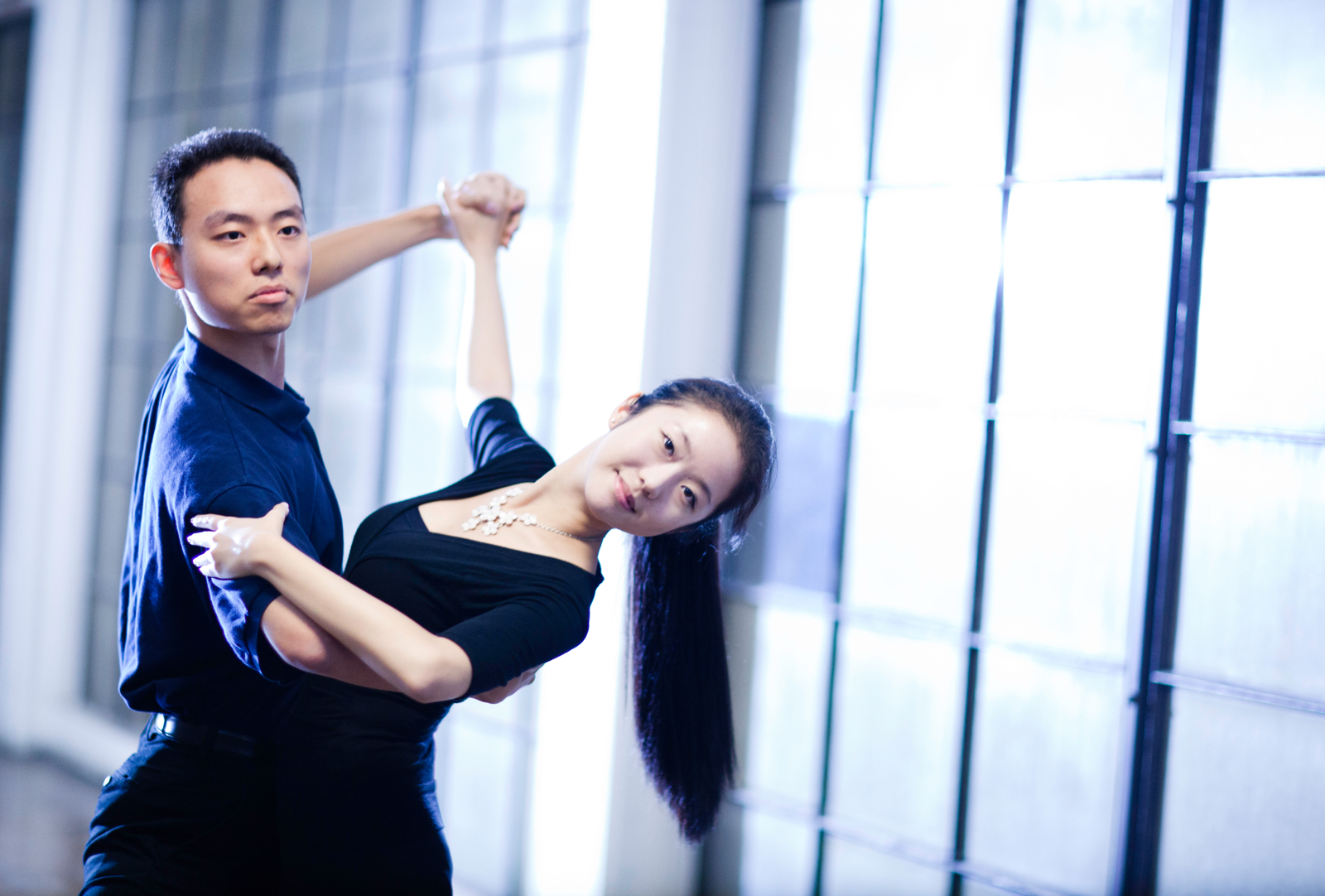 Photo of two students ballroom dancing. The male is wearing a dark blue shirt and dipping the female, who is wearing a black dress.