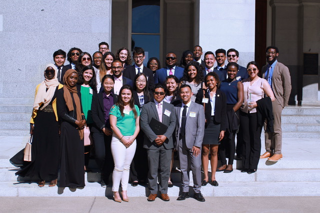 Photo of a diverse group of approximately 30 people standing on the Doe Library steps, smiling at the camera