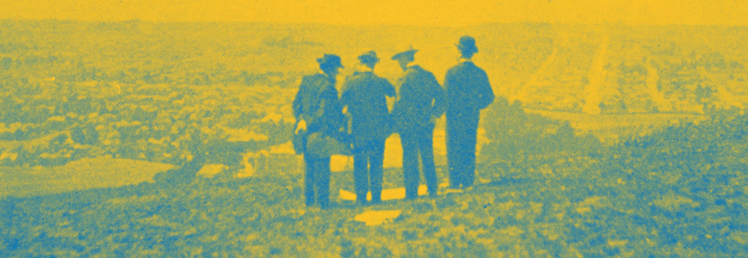 Photo of four men standing atop a hill overlooking what will some day become the campus.