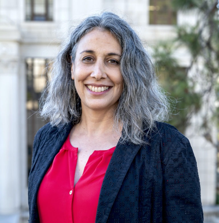 Professional headshot of Anand, who is wearing a red top and black jacket.