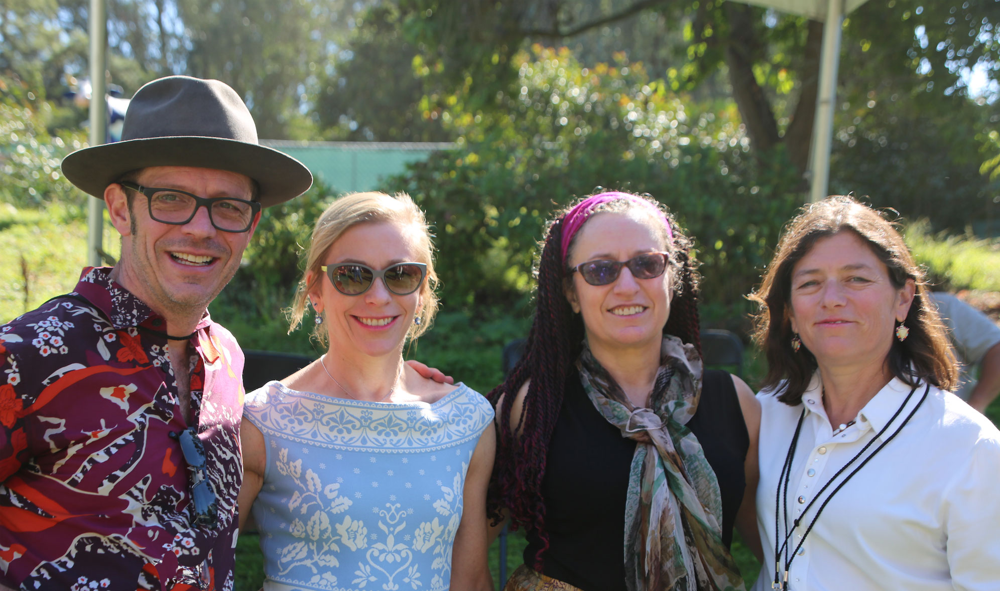 The four siblings are standing with their arms around each other and smiling.