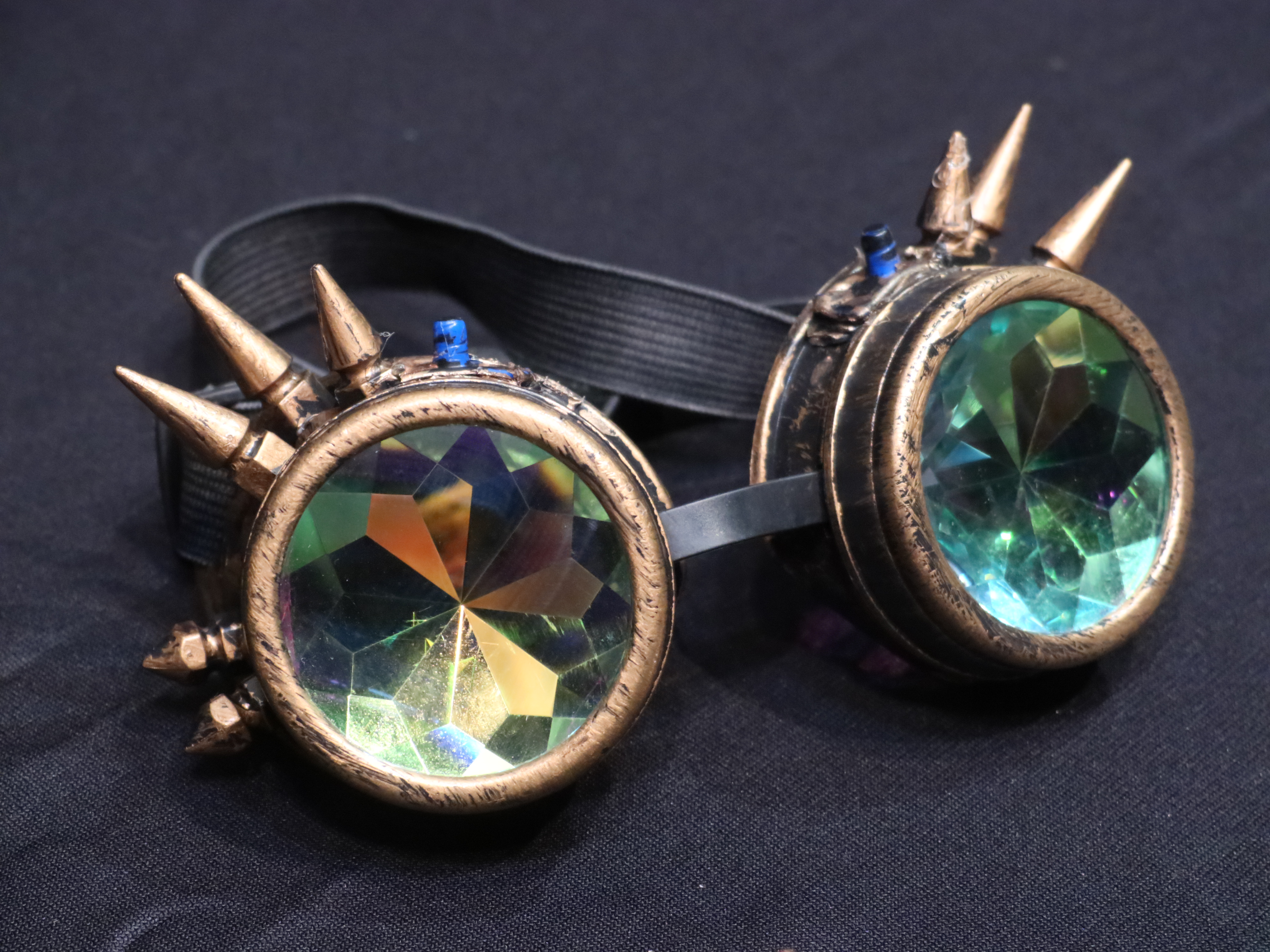 Closeup photo of bronze-rimmed goggles with spikes coming out of the top and multicolored, multifaceted lenses.