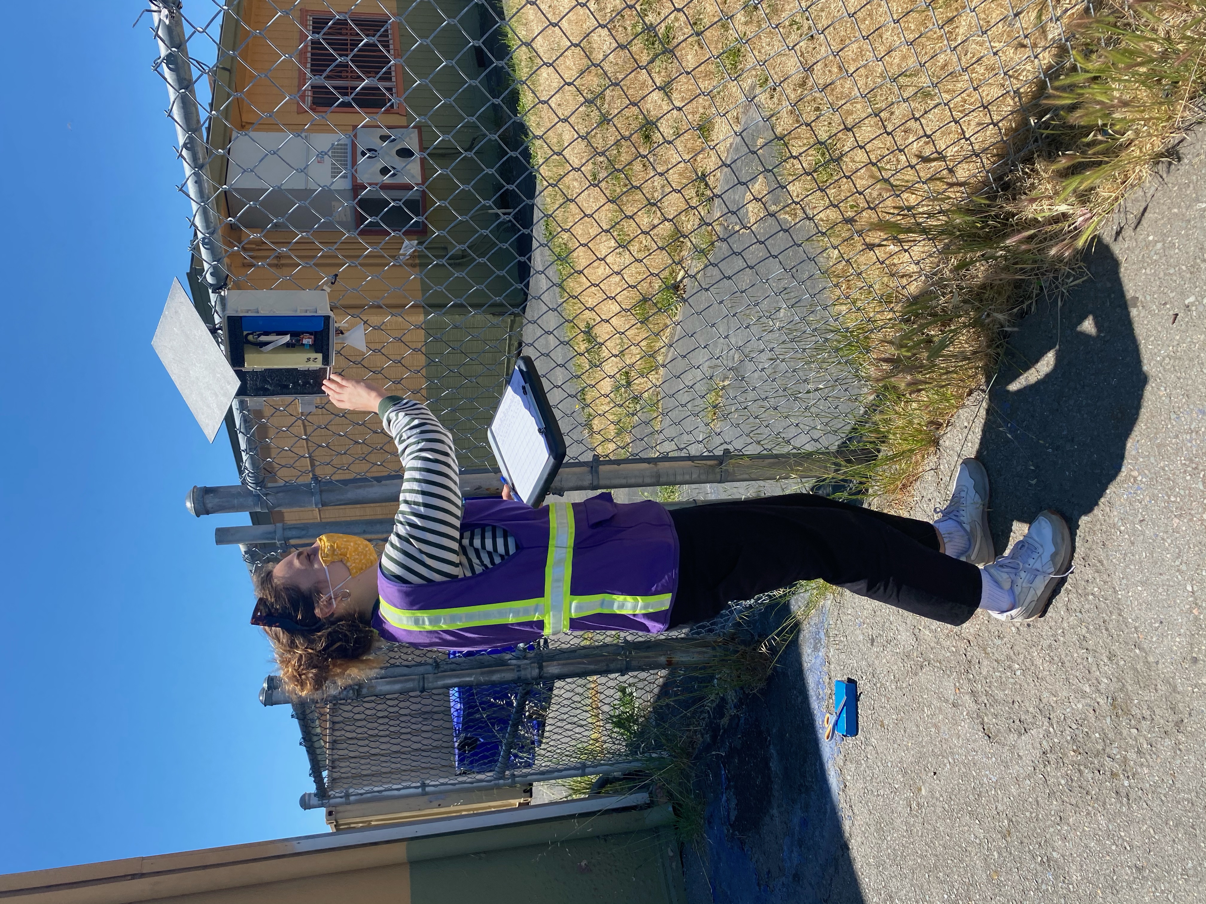 Photo of Redon-Gabel in a purple safety vest standing in front of a chain-link fence and checking a sensor.