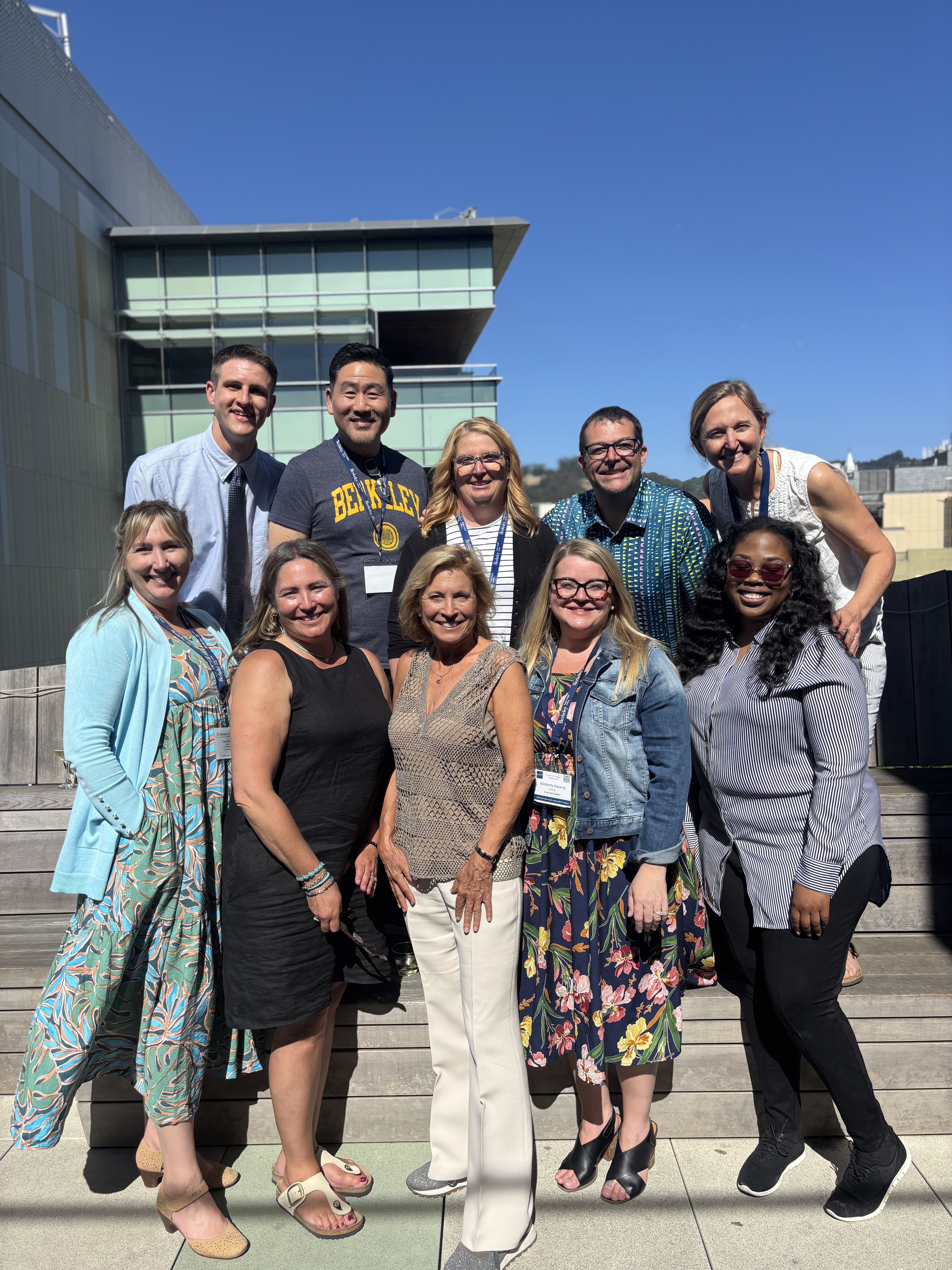Photo of a group of 10 people in two rows on steps with a building behind them and blue sky above.