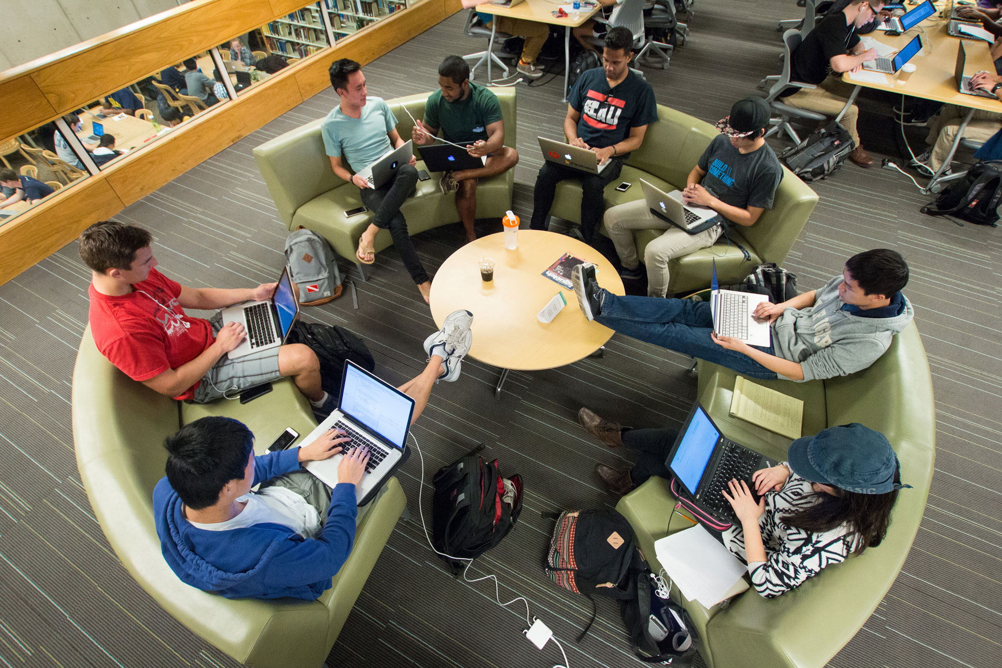 Photo of eight students sitting in a circle around a table working on laptops.