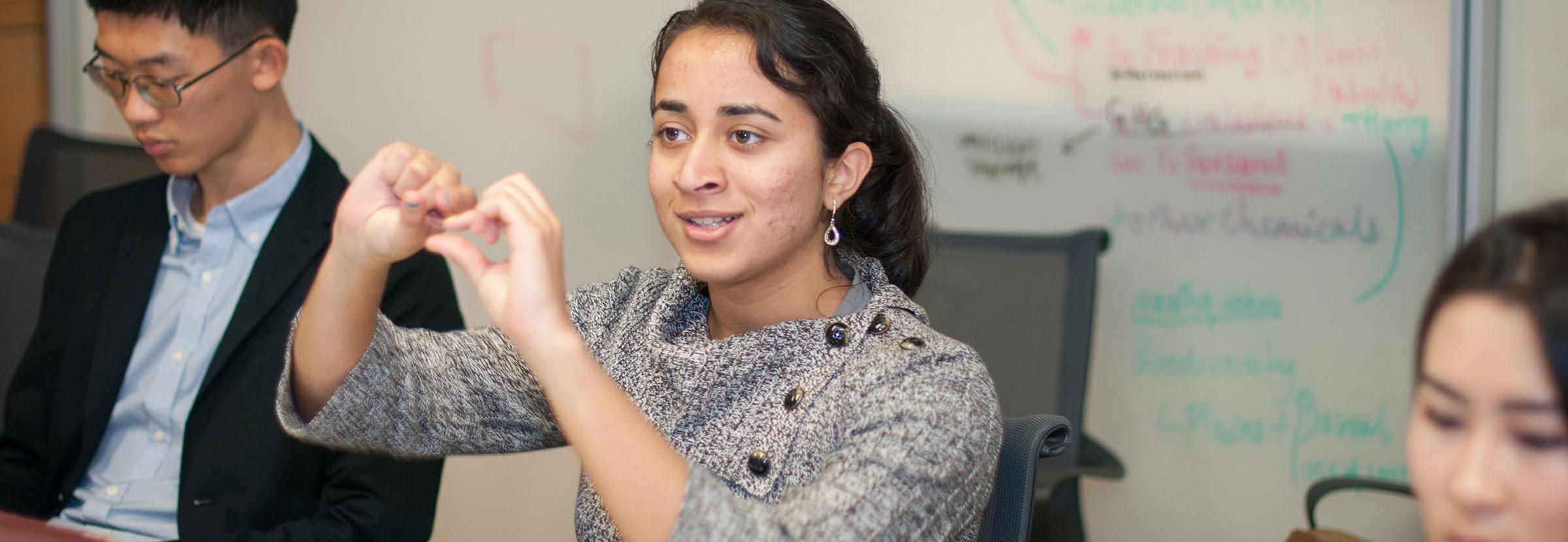 Color photo of three students, one in the middle making a hand gesture as if explaining something