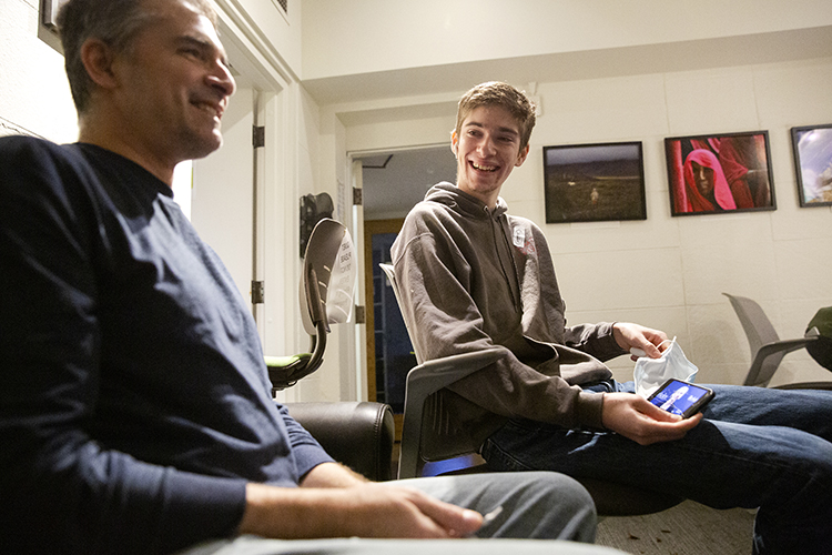 Photo of Jamie in a dark sweater smiling with Andy to his left, showing him an image of Jennifer.