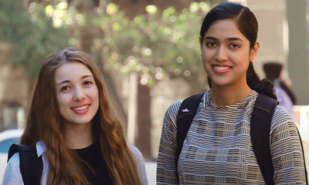 Photo of Janaki and Revekka on campus wearing backpacks with trees in the background.