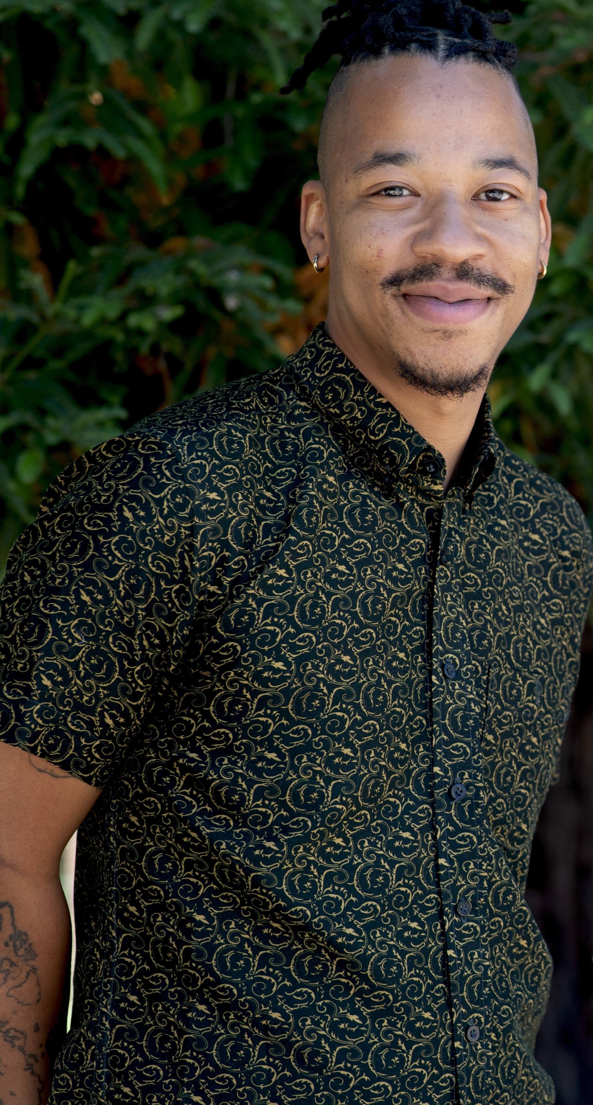 Photo of Jariel, a Black man with a mustache and goatee in a black and yellow paisley shirt