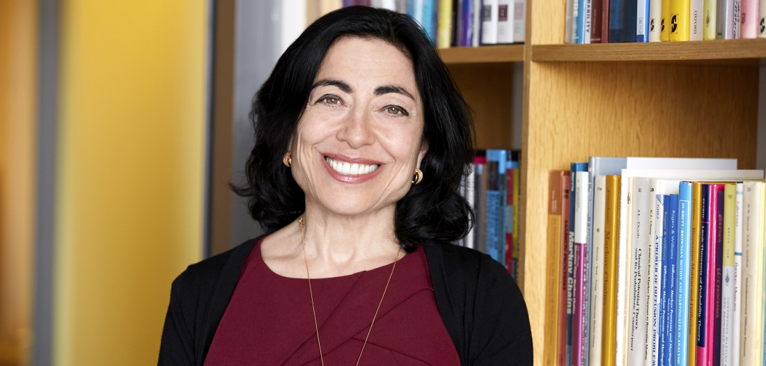 Close-up color photo of a woman smiling into the camera, bright gold walls and full bookshelves behind her