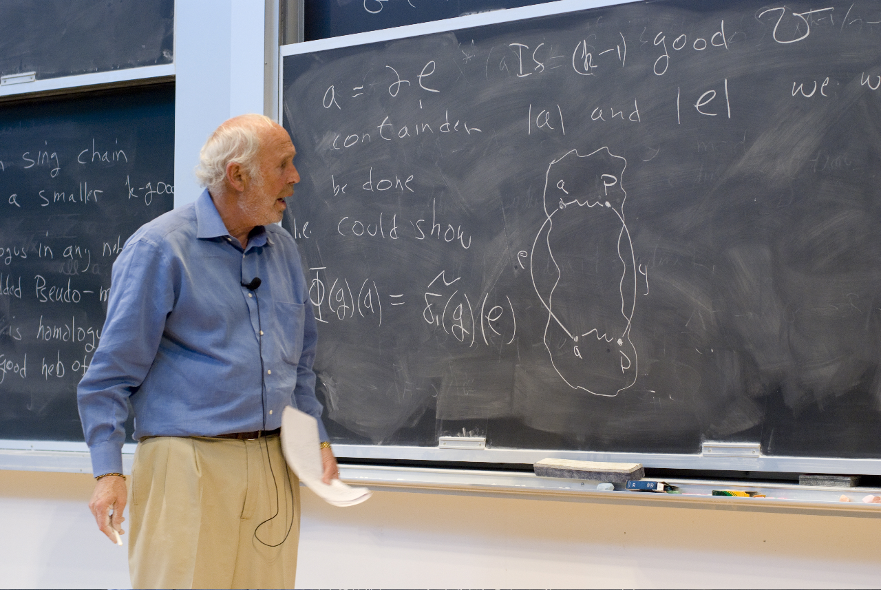 Color photo of Jim Simons standing at a chalkboard covered with words, numbers, and a diagram.