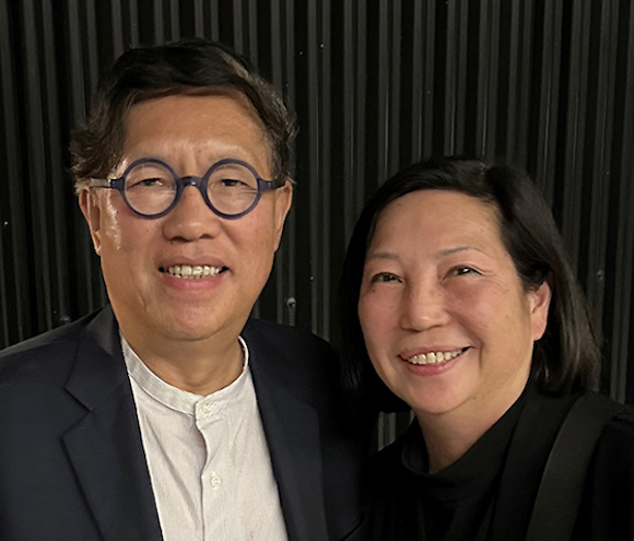 Photo of Joe and Vivian, both wearing black and standing against a black backdrop.