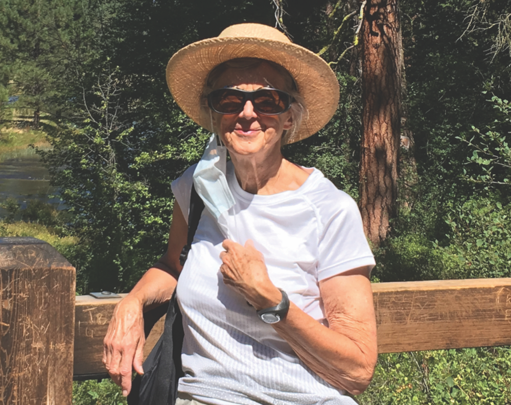 Photo of Julia in a white shirt, sunhat and sunglasses, leaning against a wooden fence.