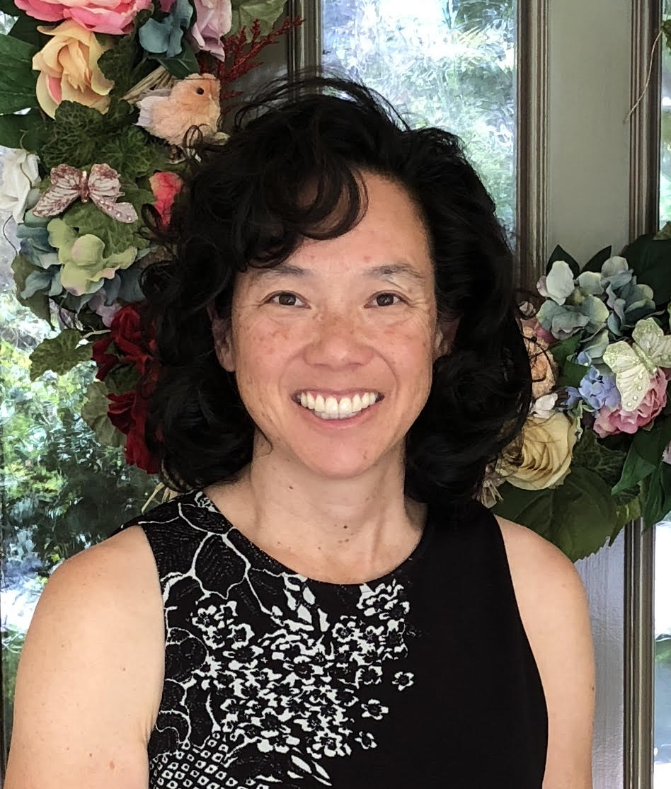 Photo of a woman smiling into the camera, a colorful wreath of flowers partially visible behind her