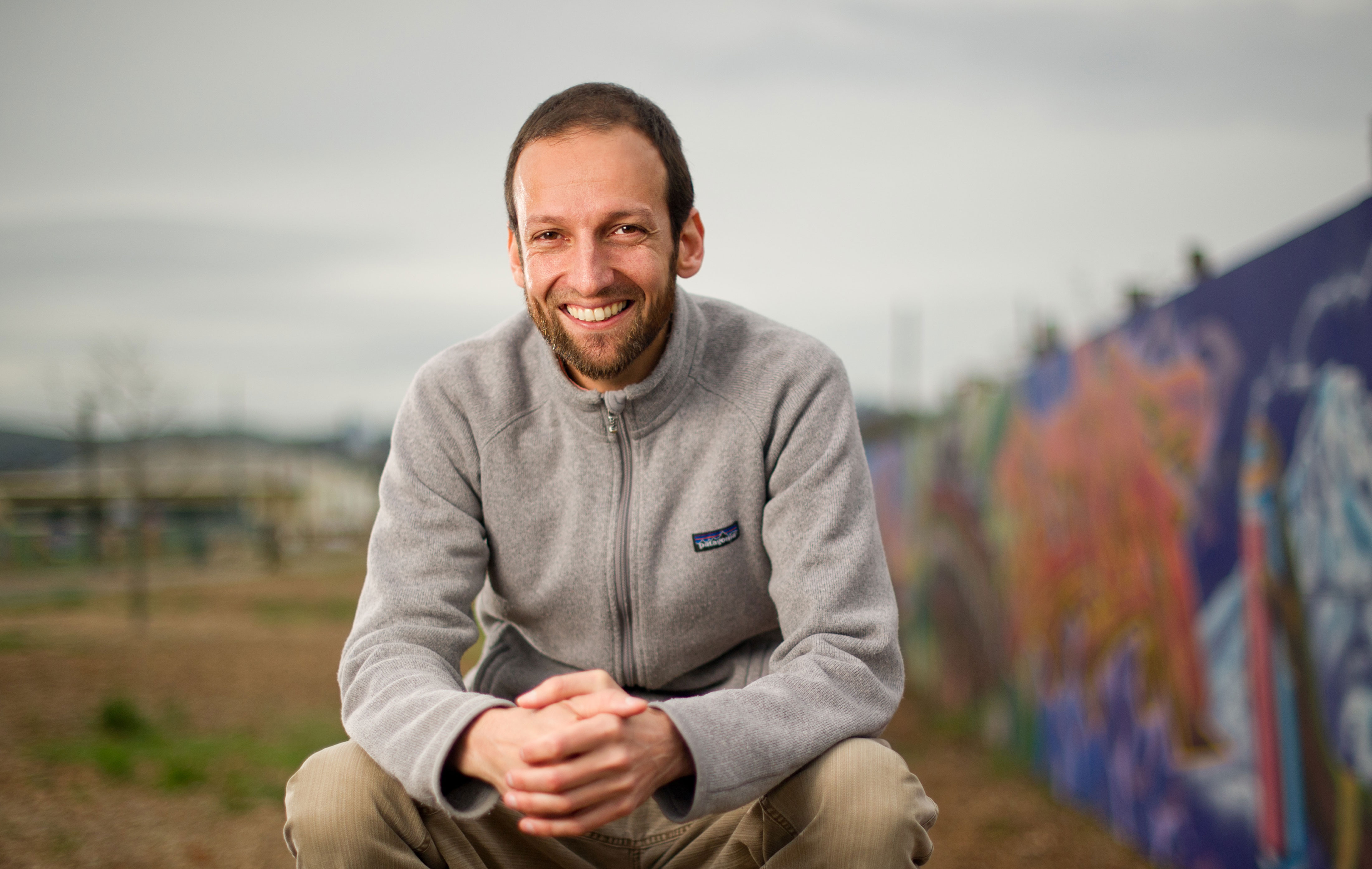 Photo of Kadir kneeling in front of a community mural.