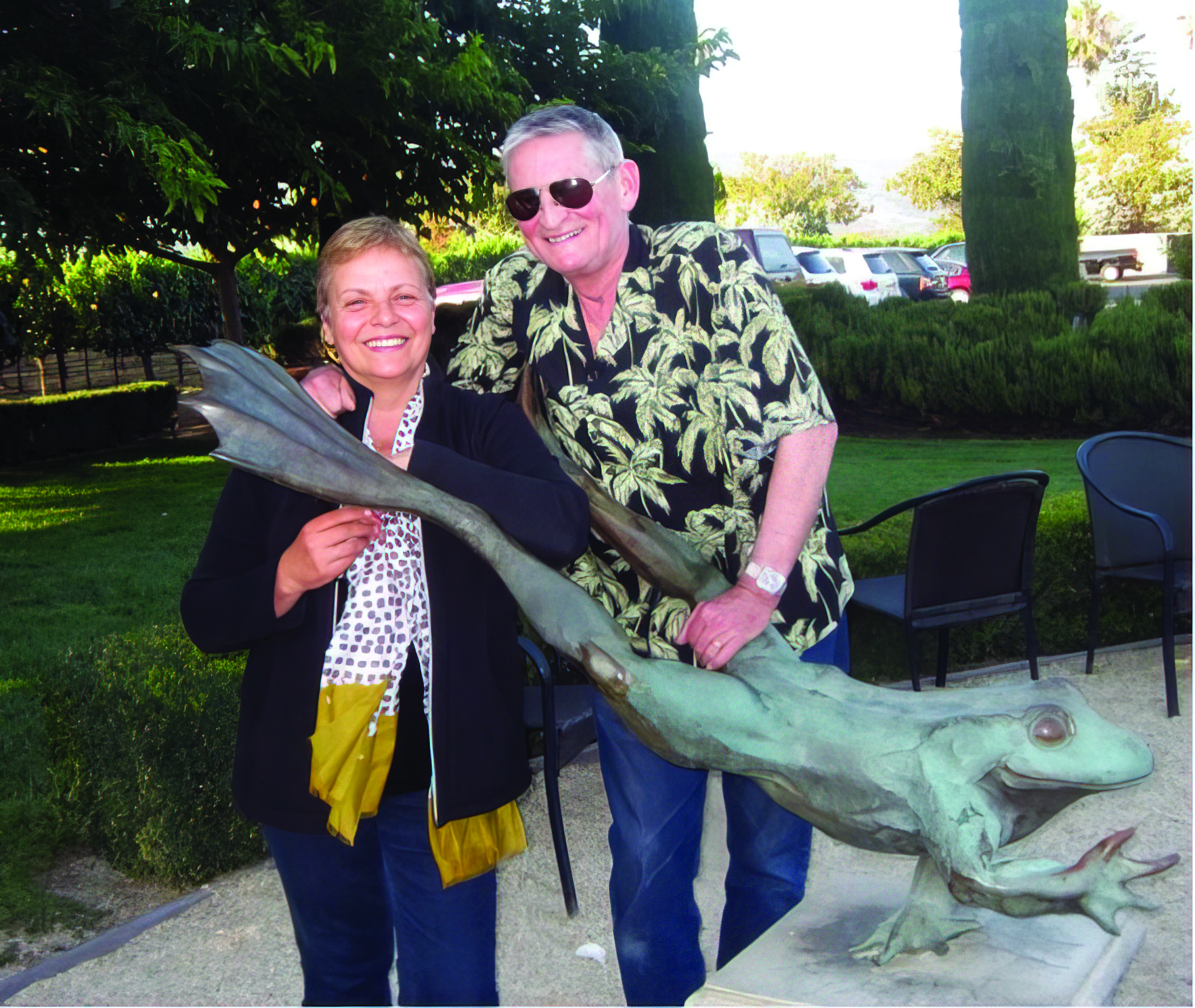 Photo of Donna, wearing a dark jacket and polka dot scarf, and Bob in a Hawaiian shirt, standing next to a statue of a frog.