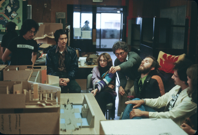 A color photo shows Lifchez crouching down and pointing to a architectural model, surrounded by at least six students.