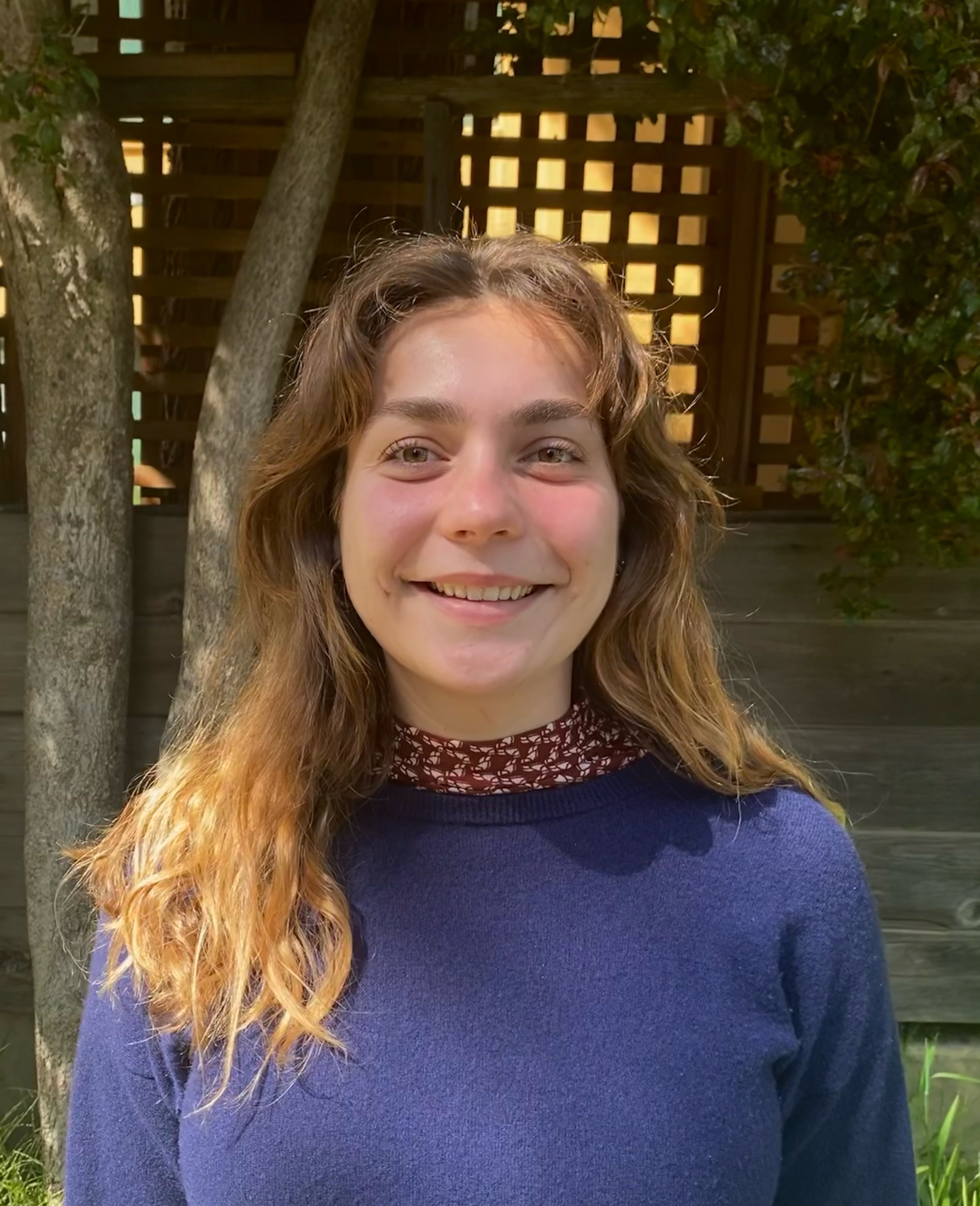 Photo of Lilu smiling with long, sandy brown hari and a purplish blue top.