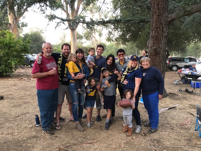 Photo of 13 members of the family, including a few cubs, huddled together in blue and gold clothes and one rogue Stanford tshirt.