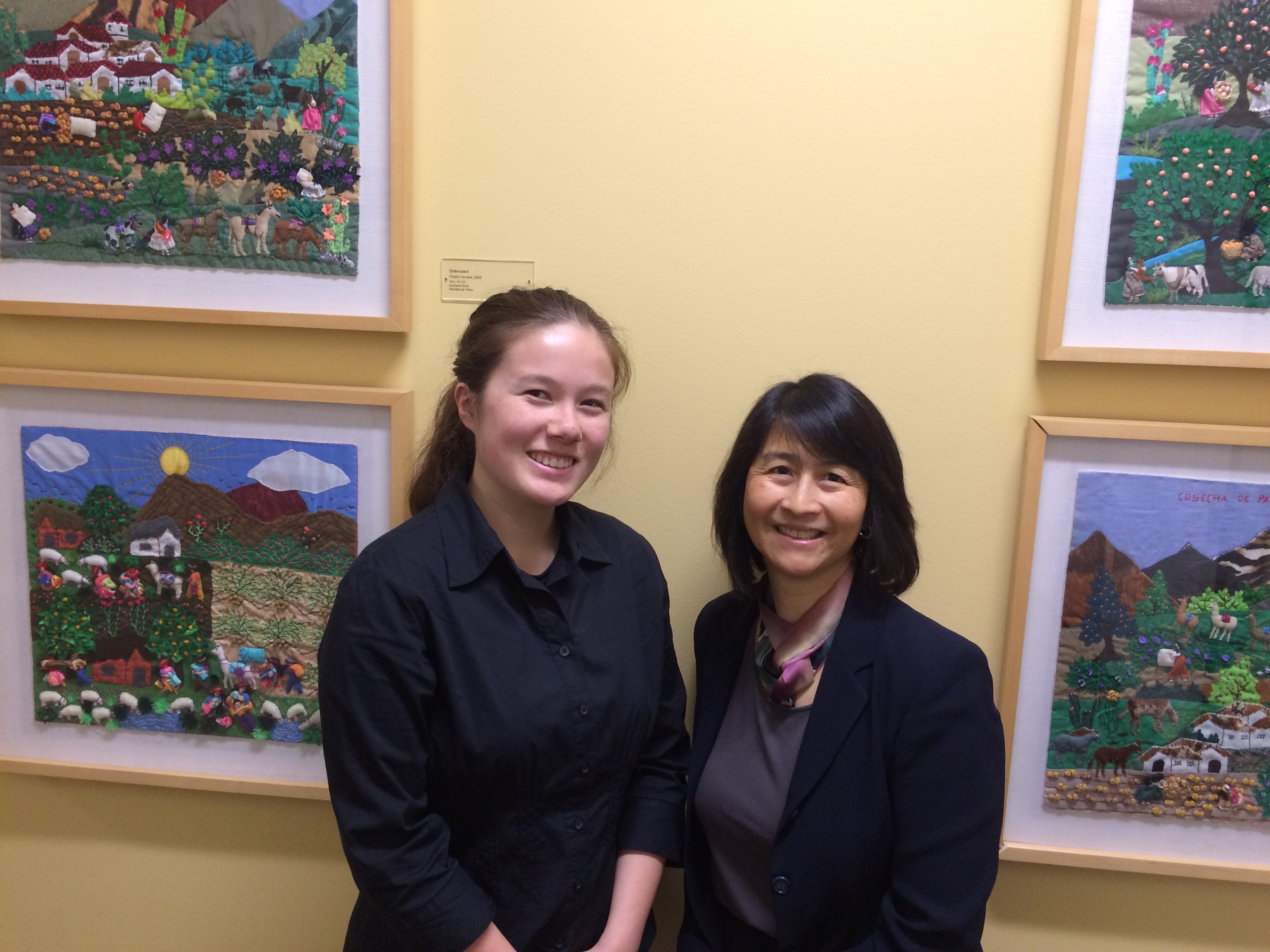 Photo of two women smiling into the camera, with paintings hung on a pale gold wall behind them