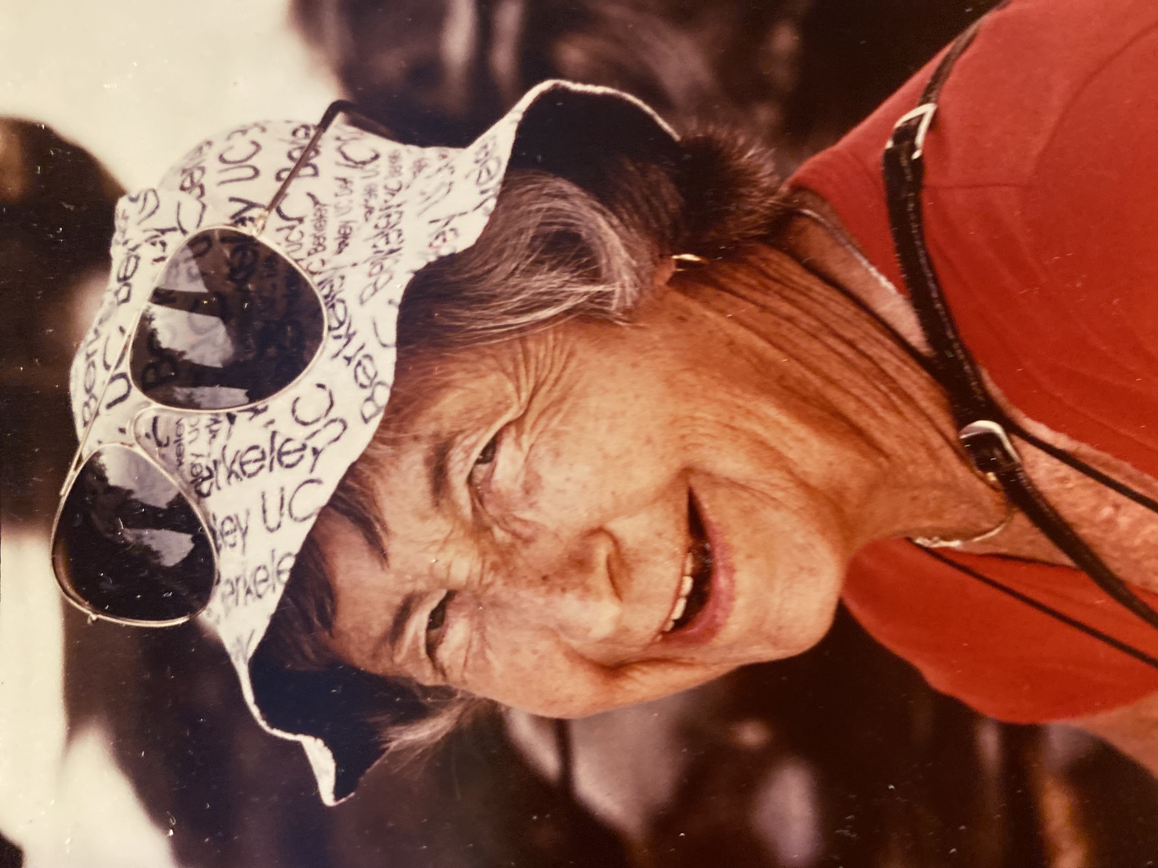 Color headshot photo of a woman smiling at the camera in a white fishing hat, sunglasses atop her head