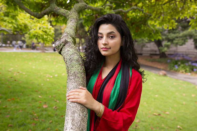 Photo of Maryam embracing a tree in a bright red shirt with a scarf that is black, red, and green.