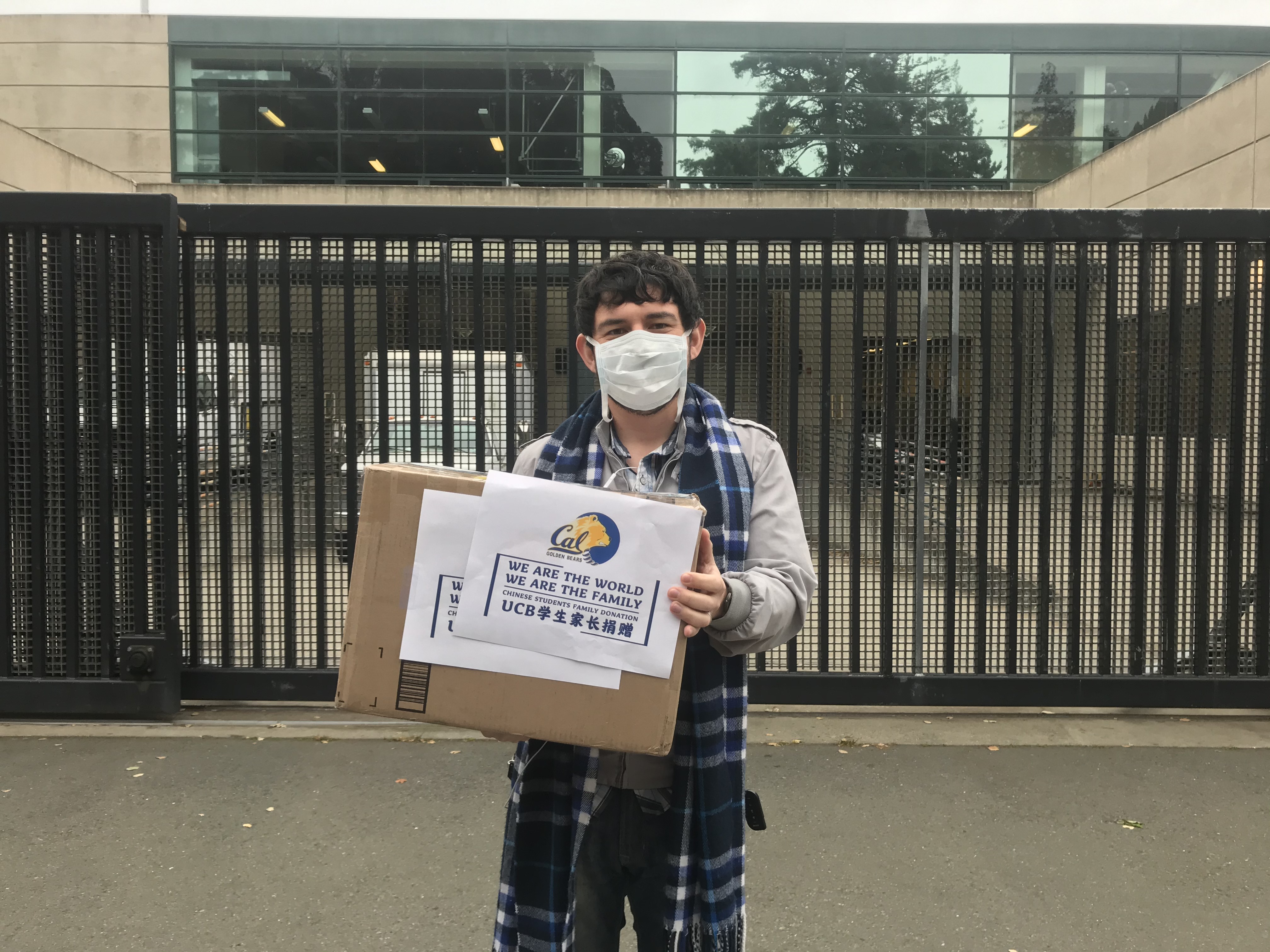 Photo of Armando wearing a mask and holding a box with a sign that says, "We are the world. We are the family. Chinese students family donation.