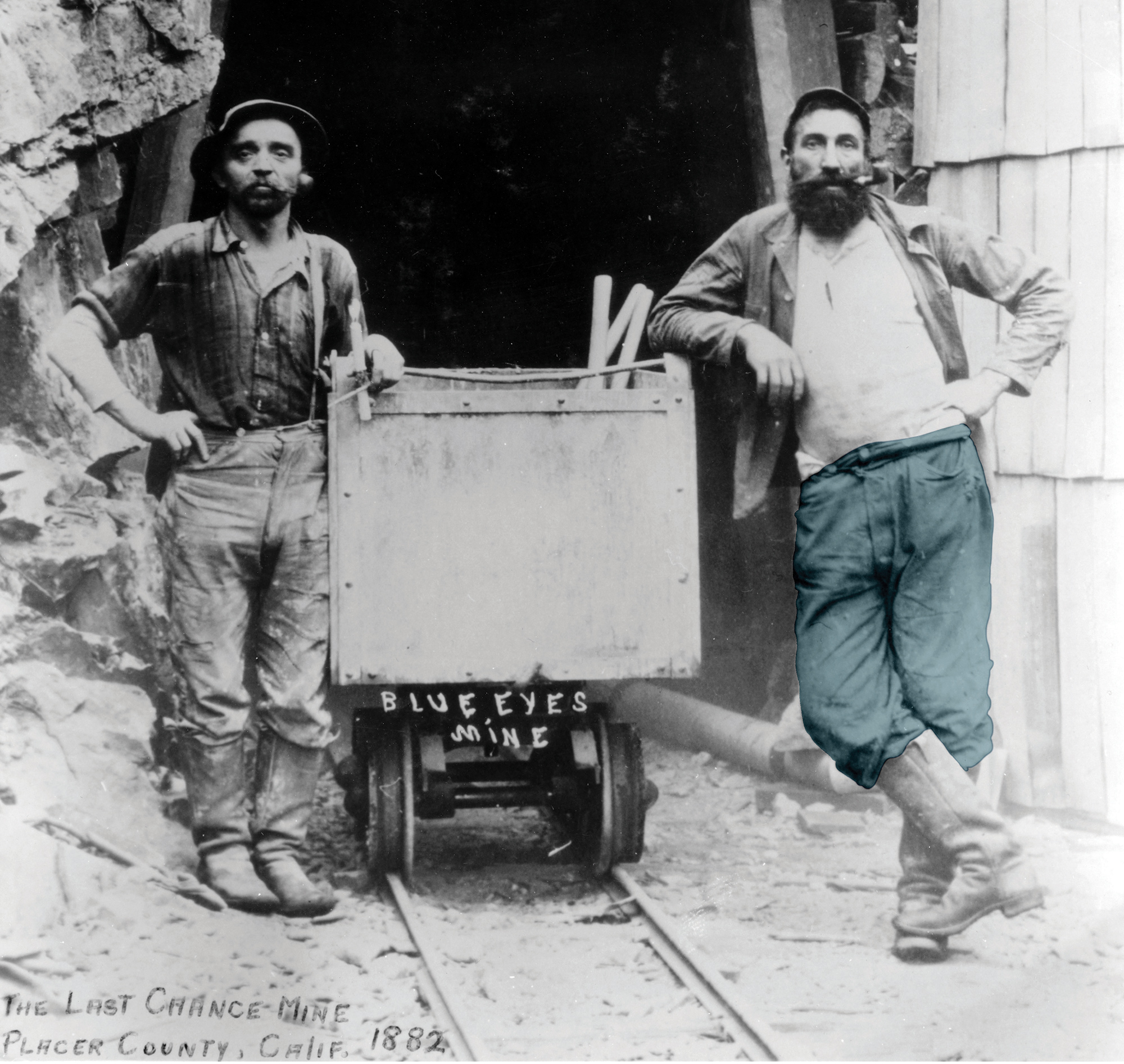 Black and white photo of two miners standing alongside a mine trolley at the mouth of the mine.