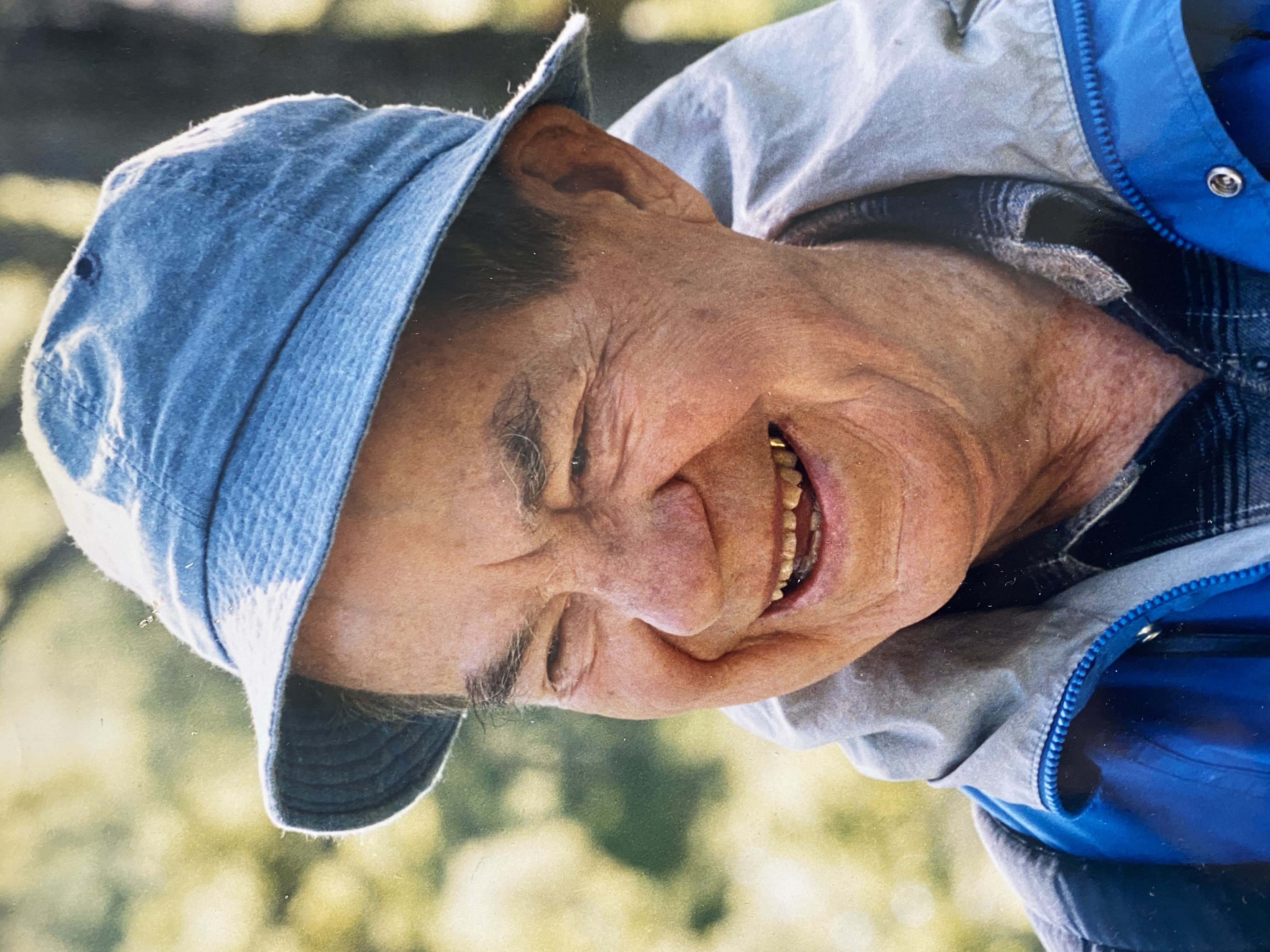 Color headshot photo of a man in a blue fishing hat, smiling at something out of frame