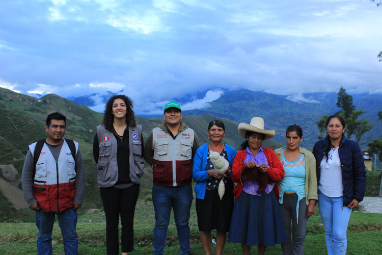 Color photo of seven people looking at the camera, most smiling, cloud-shrouded mountains in the backrgound