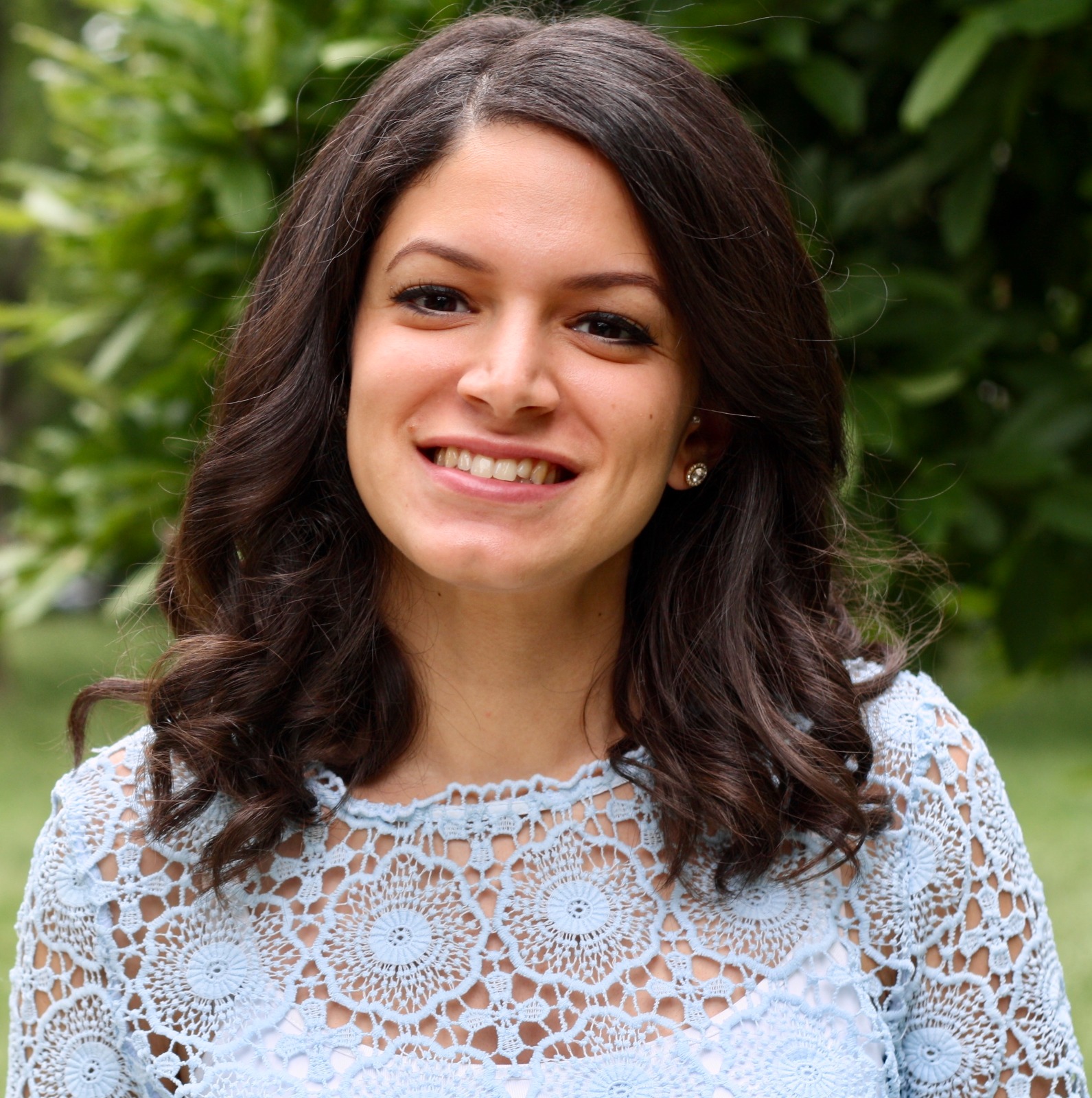 Photo of Nehal in a lacy white top with long, brown hair and smiling.