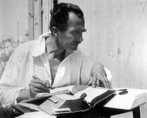 Black and white photo of Nikos, in a white button-up shirt, poring over books.