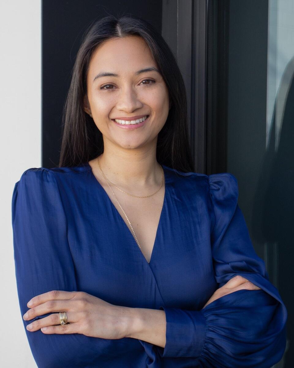 Photo of Patricia smiling with long, straight black hair, a blue top, and her arms crossed.